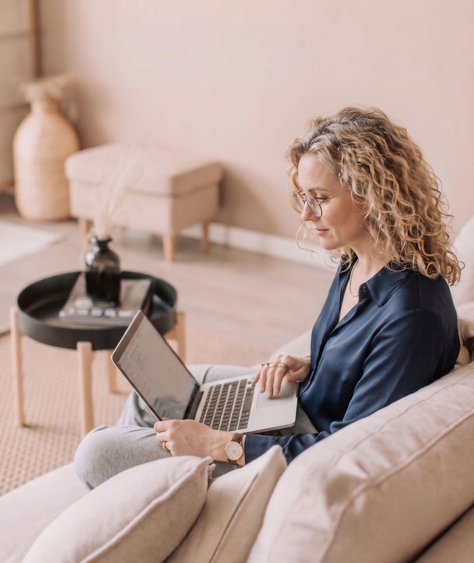 A woman working on a laptop on a sofa in a warm, naturally lit room